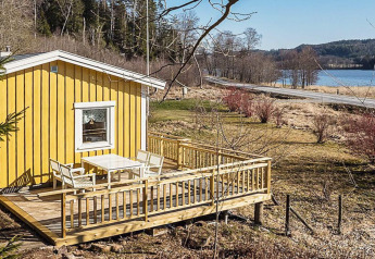 Gele vakantiehuisje met houten terras aan een meer en weg in Hällevadsholm, Zweden, landelijke omgeving.