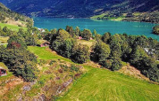 Blick auf ein grünes Tal mit See, Bergen und Holzhütten nahe Olden von einem Chalet in Dänemark.