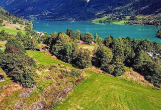 Udsigt over grøn dal med sø, bjerge og træhytter nær Olden fra en feriebolig i Danmark.