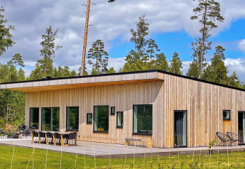 Villa spacieuse et moderne au bord d’un lac avec sauna, bardage bois et grandes fenêtres en pleine nature.