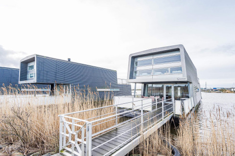 Moderne woonboot genaamd 6-persoons vakantiehuis in Hemmet, aan het water met steiger en riet.