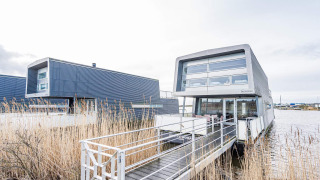 Moderne husbåd kaldet 6 personers feriehus i Hemmet, placeret ved vandet med gangbro og siv.