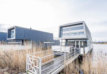 Modernes Hausboot mit dem Namen 6 Personen Ferienhaus in Hemmet, am Wasser mit Steg und Schilf.