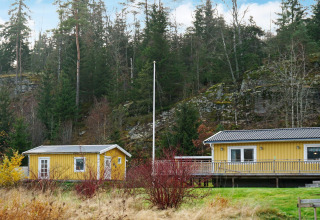 Gele vakantiewoning en bijgebouw in Hällevadsholm, Zweden, omringd door bos en rotsachtige heuvels.