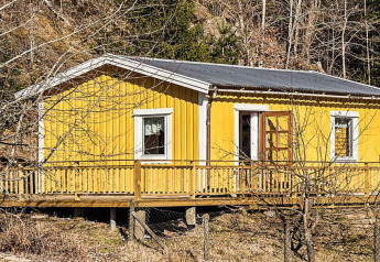 Gul træhytte kendt som '4 personers feriebolig i HÄLLEVADSHOLM' beliggende i et skovområde i Sverige.