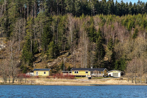 En gul hytte ved søbredden omgivet af skov i Hällevadsholm, Sverige, perfekt til en fredelig ferie.