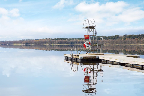 Flydende badebro med redningskrans og udspringstårn spejler sig i en stille sø nær Hällevadsholm, Sverige.