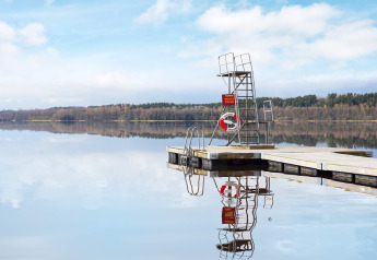 Flydende badebro med redningskrans og udspringstårn spejler sig i en stille sø nær Hällevadsholm, Sverige.