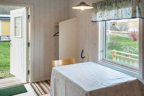 Geöffnete Tür und Tisch mit Tischtuch in einem Ferienhaus in Hällevadsholm, Schweden, mit Gartenblick.