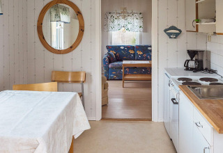 Cucina e sala da pranzo con tavolo, sedie, specchio e vista su soggiorno con divano floreale in Svezia.
