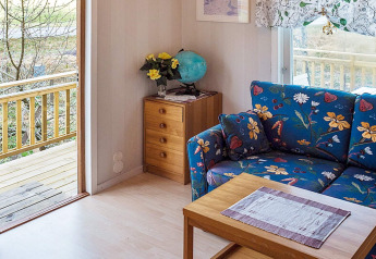 Stue i hytte i Hällevadsholm, Sverige, med farverig sofa, træbord, kommode og udsigt til veranda.