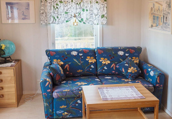 Wohnzimmer in einer Hütte mit blauem Blumensofa, Holztisch, Kommode mit Globus und Fenster.