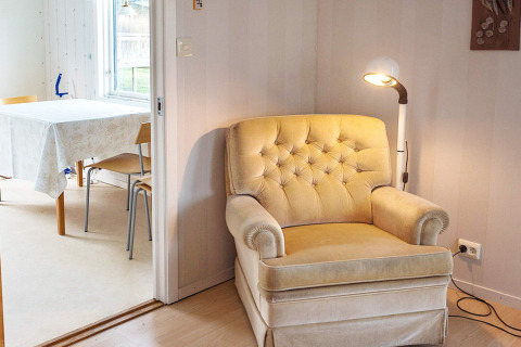 Soggiorno accogliente con poltrona beige e lampada, tavolo da pranzo visto in una baita di Hällevadsholm.