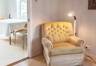 Gezellige zithoek met beige fauteuil en lamp, eettafel en stoelen in vakantiehuis Hällevadsholm.