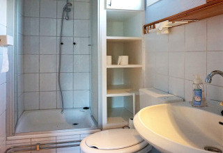 Compacte badkamer met douche, toilet, wasbak en schappen in een 4-persoonshuisje in Hällevadsholm, Zweden.