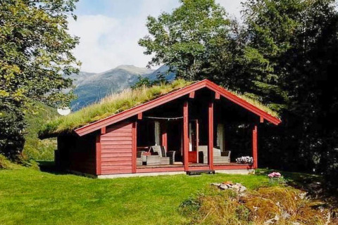 Rood houten chalet met grasdak, omgeven door bomen en bergen in Olden, Denemarken, op een zonnige dag.