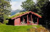Chalet rojo de madera con techo de césped, rodeado de árboles y montañas en Olden, Dinamarca, en día soleado.