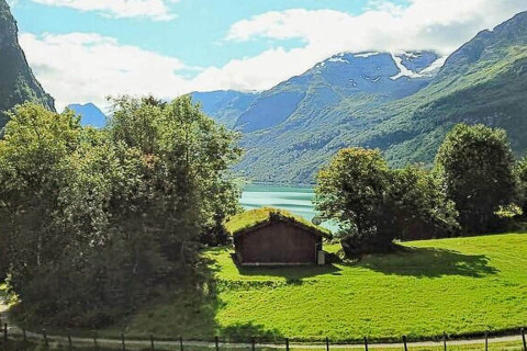 Blick von einem Ferienhaus in Olden, Dänemark, mit grünen Wiesen, Bäumen, Bergen und See im Hintergrund.