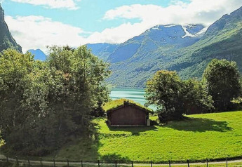 Uitzicht vanuit een vakantiehuisje in Olden, Denemarken, met groene velden, bomen, bergen en een meer op de achtergrond.