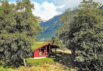 Chalet rosso per sei persone a Olden, Danimarca, immerso tra alberi e montagne panoramiche.