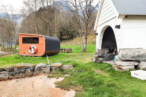 Udendørs scene ved et feriehus i Olden, Danmark, med sauna, græsplæne og bjerge i baggrunden.