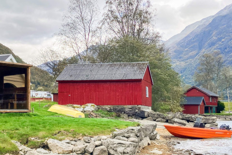 Rood houten huisje aan het meer met boot en bergen, vakantiehuis in Olden, Denemarken, landelijke sfeer.