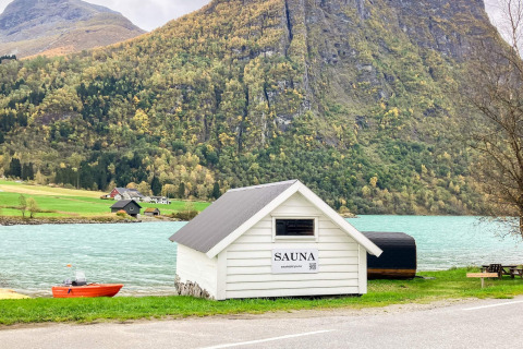 Hvid sauna ved søbred med bjerge i baggrunden, nær Sommerhus til 6 personer i Olden, Danmark.