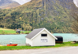 Hvid sauna ved søbred med bjerge i baggrunden, nær Sommerhus til 6 personer i Olden, Danmark.