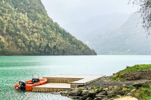Foto van een meer met een houten steiger, een oranje boot en bergen op de achtergrond in Olden.
