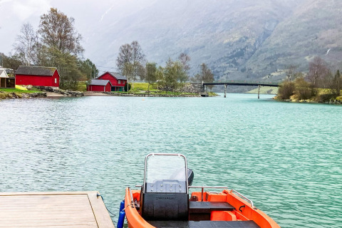 Boot aan de steiger, turquoise water, rode huisjes en bergen bij 6-persoons vakantiehuis in Olden.