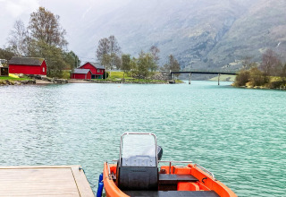 Boot aan de steiger, turquoise water, rode huisjes en bergen bij 6-persoons vakantiehuis in Olden.
