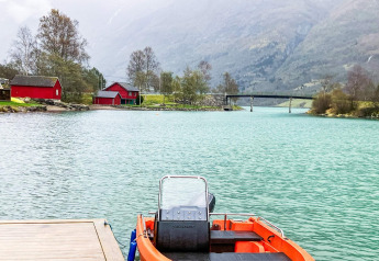 Bateau au quai, eau turquoise, cabanes rouges et montagnes près du chalet 6 personnes à Olden.