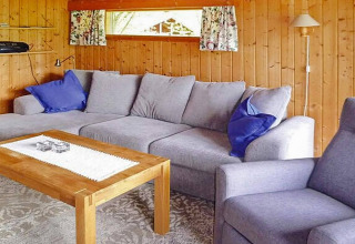 Wohnzimmer in Chalet in Olden, Dänemark mit grauem Sofa, Holzwänden, Holztisch und blauen Kissen.