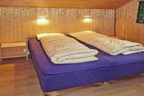 Knusse slaapkamer met tweepersoonsbed, houten wanden en lampen in een chalet in Olden, Denemarken.
