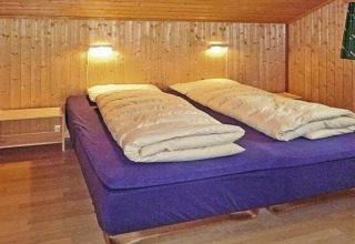 Chambre confortable avec lit double, murs en bois et lampes murales dans un chalet à Olden, Danemark.