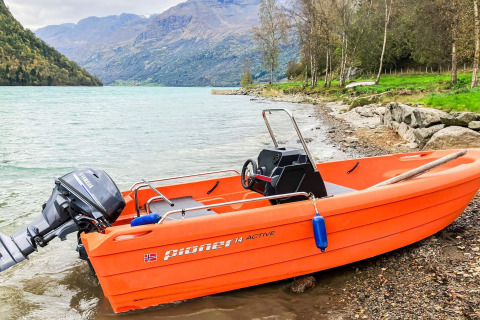 Orange motorbåd ved søbred med bjerge i baggrunden ved et sommerhus i Olden, Danmark.