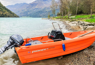 Barca a motore arancione sulla riva del lago con montagne sullo sfondo presso uno chalet a Olden, Danimarca.