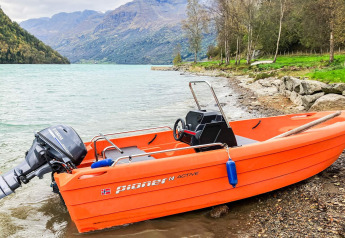 Barca a motore arancione sulla riva del lago con montagne sullo sfondo presso uno chalet a Olden, Danimarca.