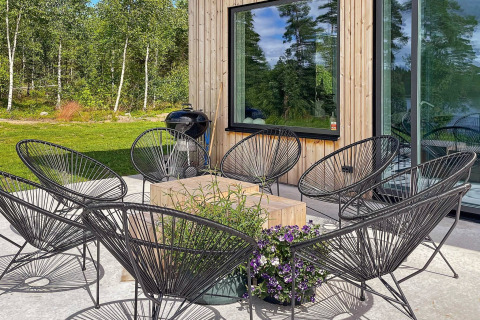 Patio esterno di una villa svedese con sedie nere, tavolo in legno, fiori e sfondo verde boscoso.