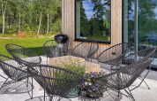 Terrasse extérieure d’un lodge en Suède avec chaises noires, table en bois, fleurs et nature verdoyante.