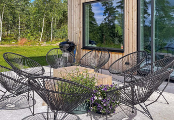 Buitenterras bij een Zweedse lodge met zwarte stoelen, houten tafel, bloemen en bosrijke achtergrond.