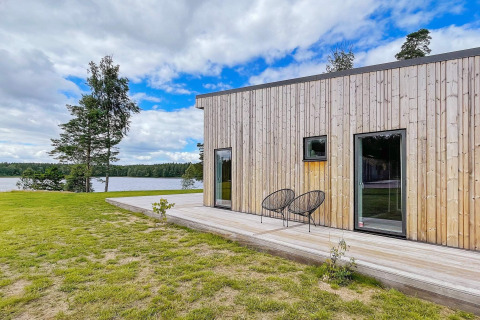 Moderne lodge aan een Zweeds meer met houten gevel, terras, stoelen en uitzicht op het water.