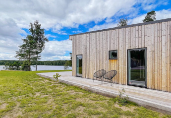 Moderne villa aan het meer in Zweden met houten gevel, terras, stoelen en uitzicht op het water.