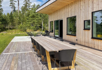 Buitenterras bij Spacious Lakeside Villa met houten tafel, zwarte stoelen en boszicht in Zweden.