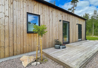 Façade en bois d'une villa spacieuse au bord d'un lac en Suède, avec terrasse en bois et cadre naturel.