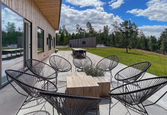 Terrasse extérieure avec chaises noires modernes à la Spacious Lakeside Villa en Suède, entourée d’arbres.