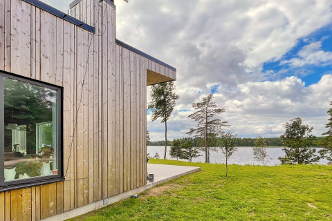 Moderna villa in legno sul lago in Svezia, con grandi finestre e vista su acqua e foresta circostante.