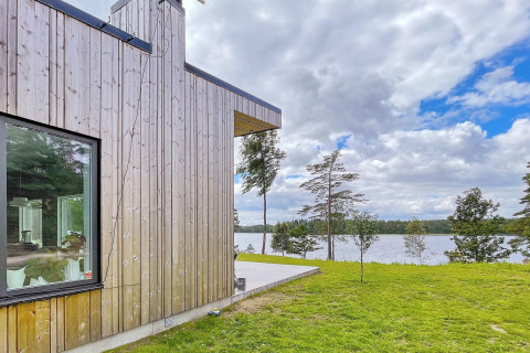 Moderna villa in legno sul lago in Svezia, con grandi finestre e vista su acqua e foresta circostante.
