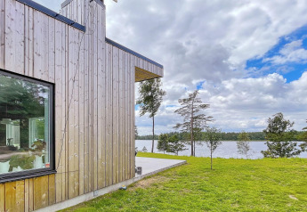 Moderne houten villawoning aan het meer in Zweden, met grote ramen en uitzicht op water en bos.