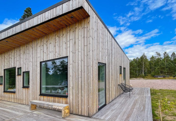 Moderna villa junto al lago en Suecia con paneles de madera, grandes ventanales y terraza en entorno natural.